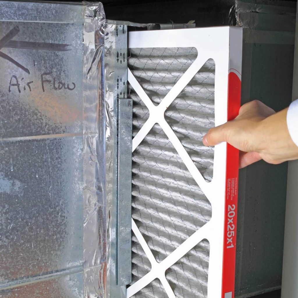 A hand pulls out an air filter from a furnace.