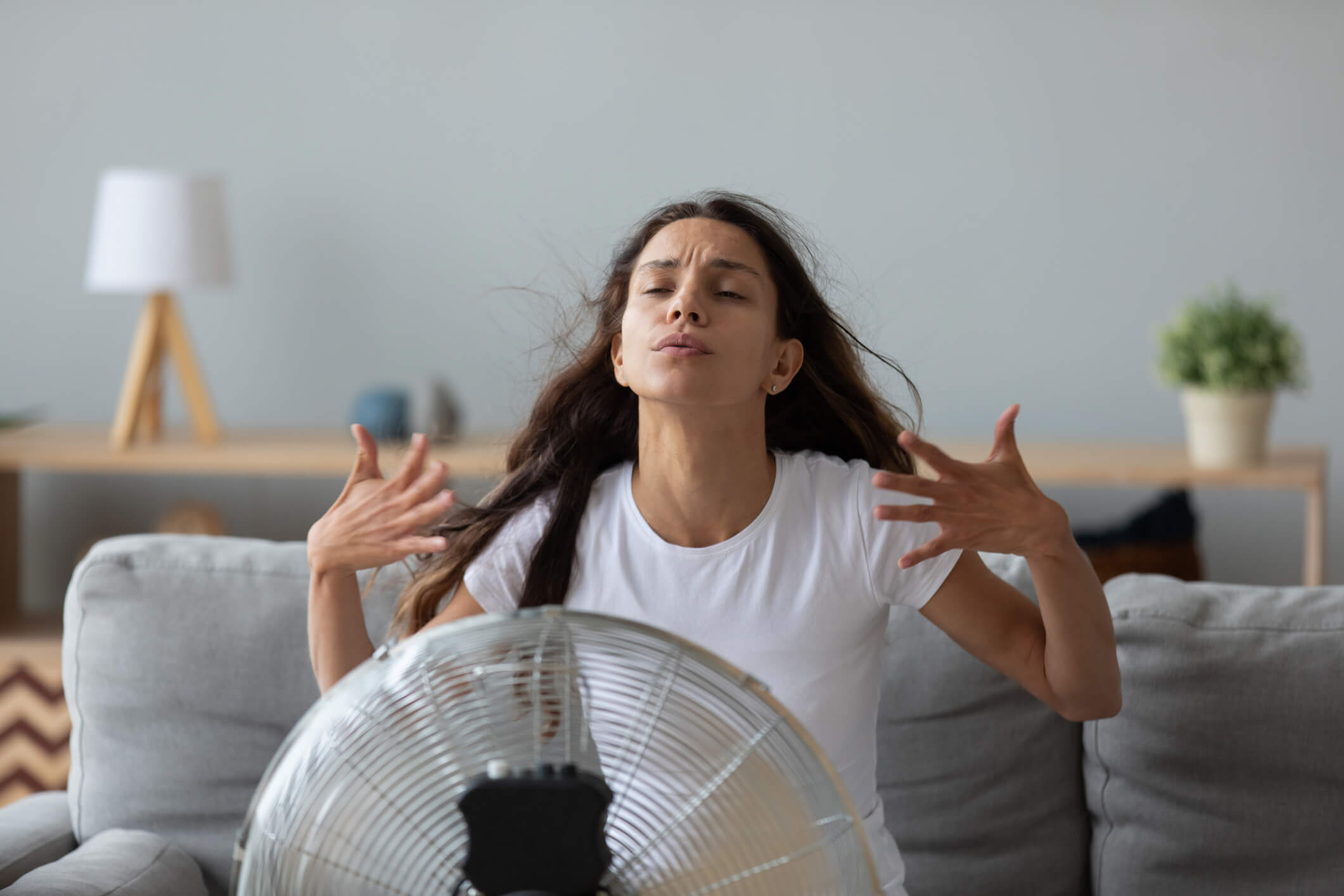 A woman sits in front of a fan trying to cool down